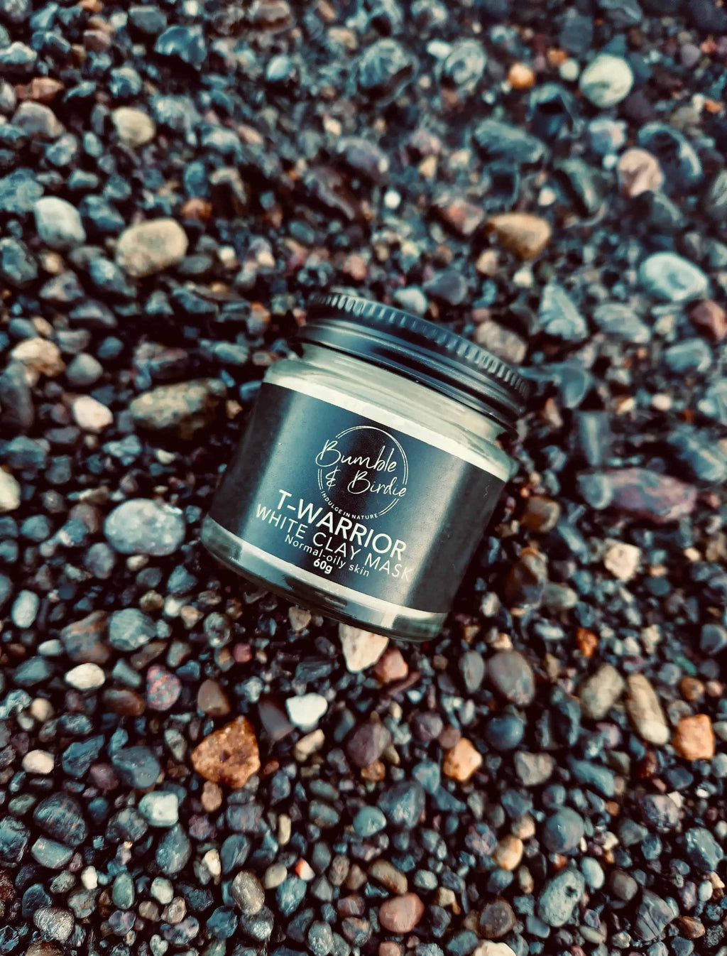 T-Warrior White Clay Mask jar lying on dark pebbles