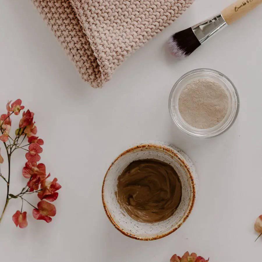 Tuned Out clay mask mixed in a speckled clay bowl, beside the open jar of powder and a mask brush
