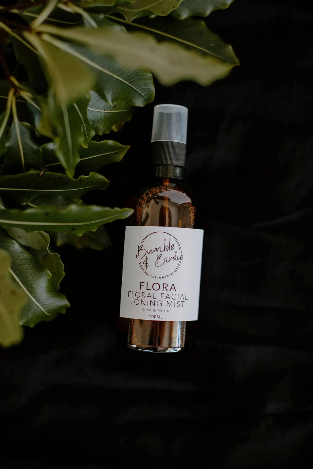 Flora facial toning mist bottle on a dark background with green leaves