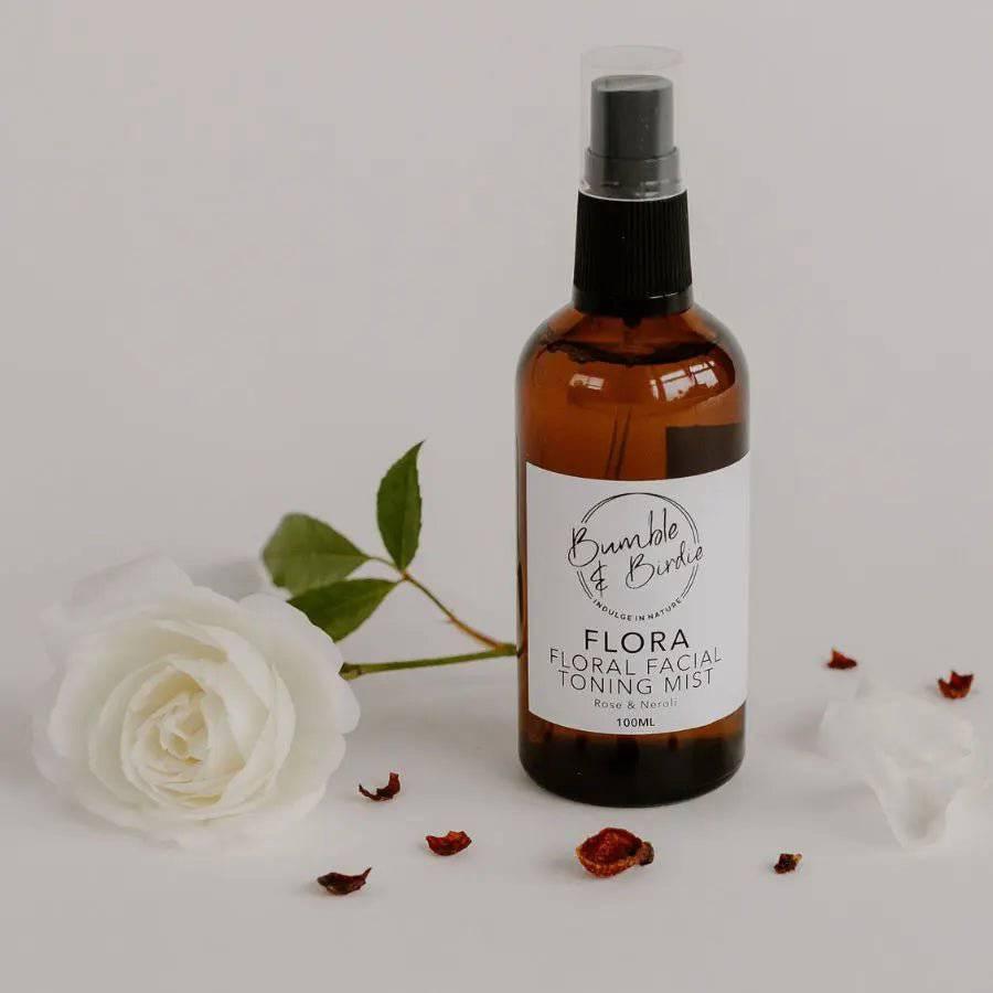 Flora facial toning mist in an amber spray bottle beside a white rose