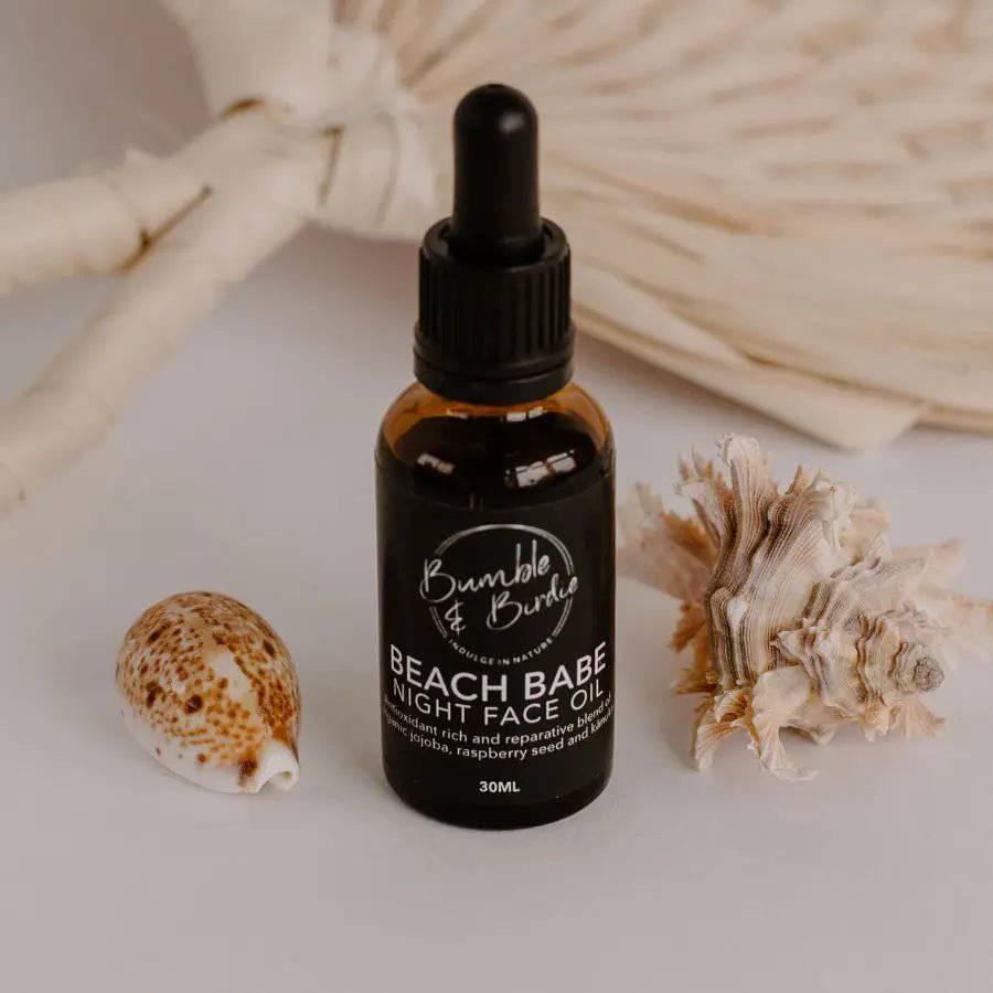 Beach Babe night face oil in a dropper bottle by Bumble & Birdie, with shells and a woven fan