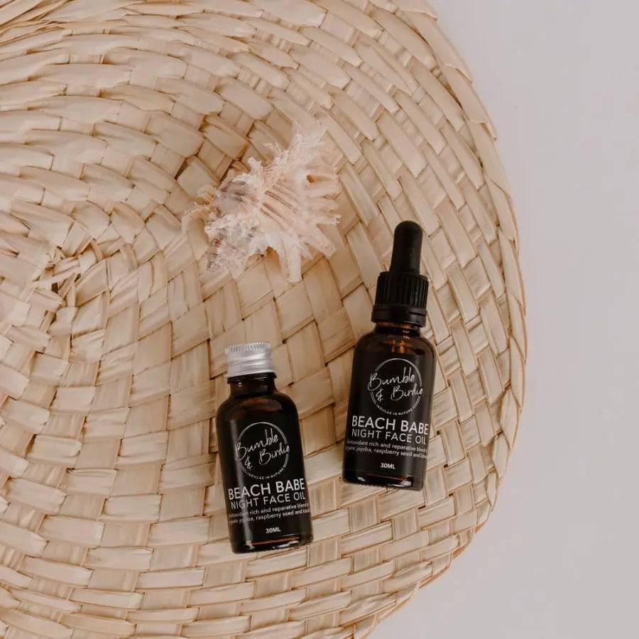 Beach Babe night face oil dropper bottle and refill bottle on a woven mat