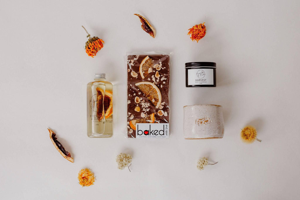 Zest of Life Selfcare Set laid out: body oil, chocolate bar, tin candle and clay bowl with dried citrus