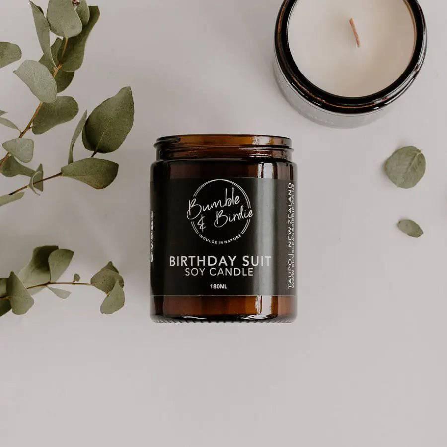 Birthday Suit soy jar candle with an open candle and eucalyptus leaves