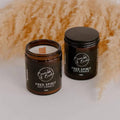 Two Free Spirit soy jar candles by Bumble & Birdie, one open with a wood wick, with pampas grass