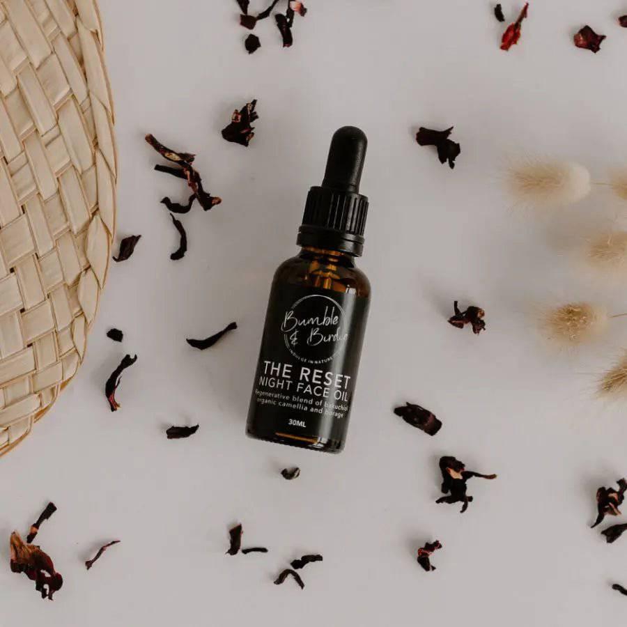 The Reset night face oil dropper bottle surrounded by dried petals