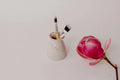 Earth Brush Haven speckled pottery vase holding face mask brushes, beside a magnolia flower