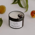 Peachy Keen soy candle in an open black tin by Bumble & Birdie, with peaches and leaves