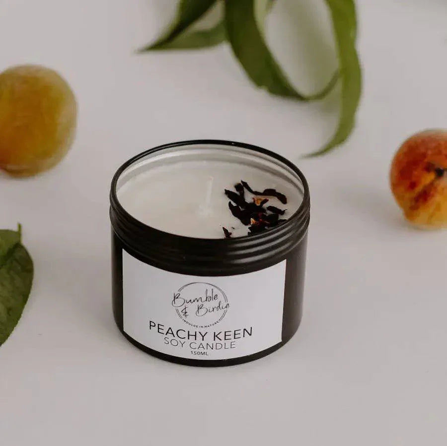 Peachy Keen soy candle in an open black tin by Bumble & Birdie, with peaches and leaves