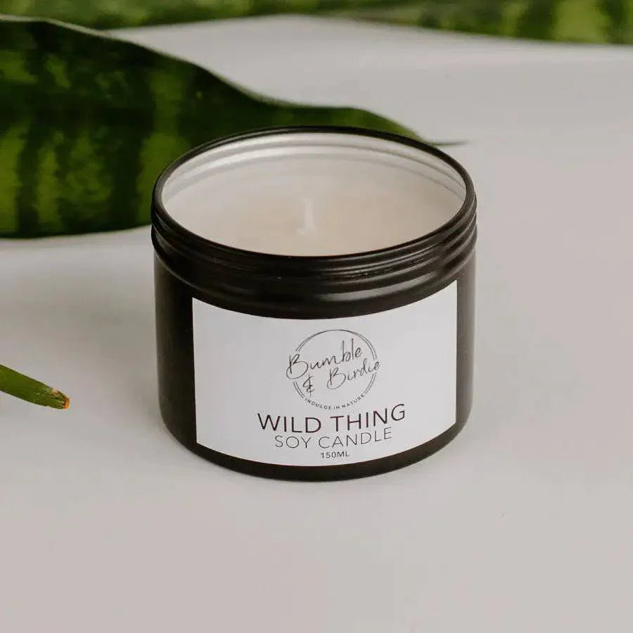 Wild Thing soy candle in an open black tin by Bumble & Birdie, with green leaves