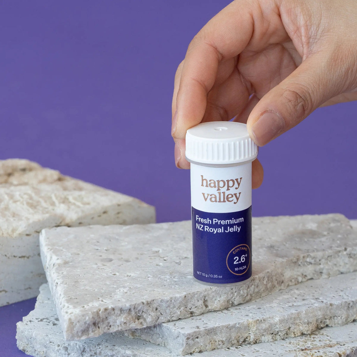 Hand holding Happy Valley NZ Fresh Royal Jelly container on stone