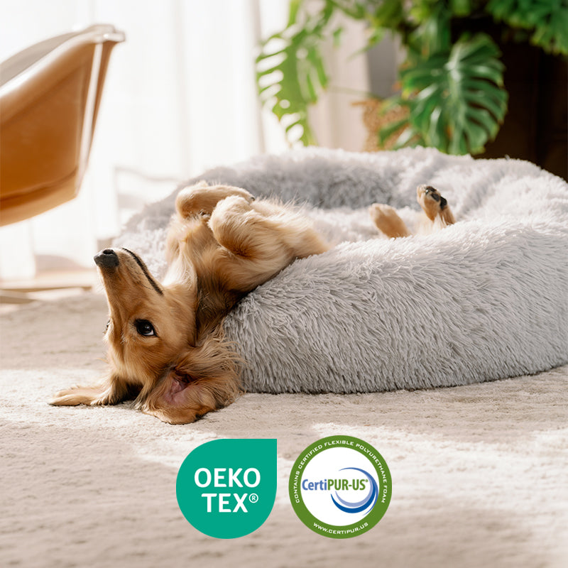Dog lying upside down on a light grey round plush Brooklyn dog bed, with fabric certification logos