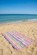 Pink and green striped Frankly Cotton beach towel on the sand by the sea